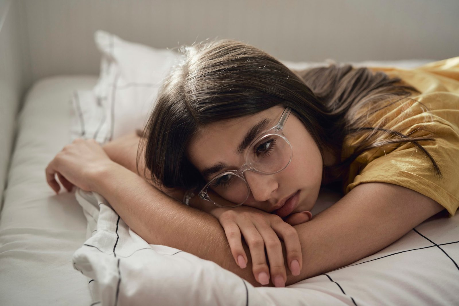 Sad caucasian teenage girl lying on bed and looking away with anxiety